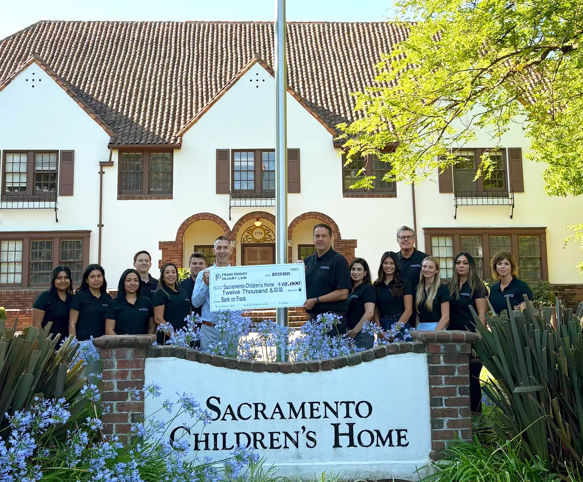 The Frank Penney Injury Law team gathered at the Sacramento Children's Home sign for the $12,000 check presentation